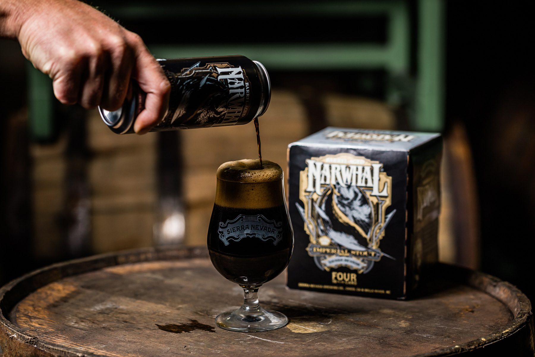 Pouring a can of Barrel-Aged Narwhal into a glass that sits atop a barrel